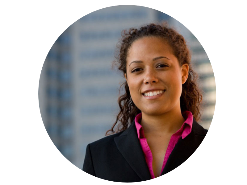 Smiling woman in black suit and pink shirt with curly hair, blurred city background.