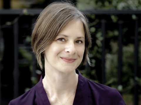 Rachel Lennon, smiling with short graying hair wearing a dark purple top, blurred green background.